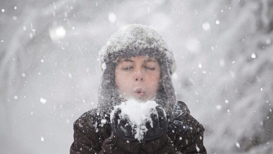 man blowing on snowball during winter